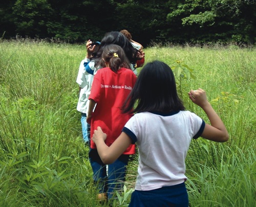 Teens walking on a path surrounded by tall grass following a leader on an adventure nature trip.