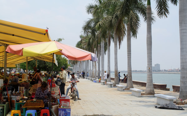 Riverfront market in Phnom Penh with cafes and people along the boardwalk.