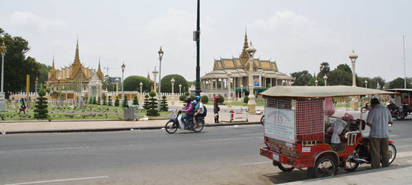 A typical scene in Phnom Penh with a tuktuk and a motorbike with temples in the background.