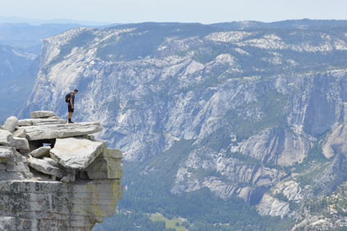 A student standing on a rocky ledge gazing down from the top of a mountain during a gap year.