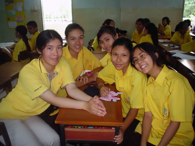 Author in Thailand working as a teaching assistant with students at a classroom table.