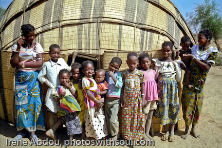 Fulani family standing in front of grass mat house.