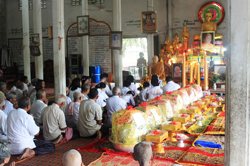 Cambodian Buddhist prayer ceremony with worshippers on their knees before a priest inside a temple.