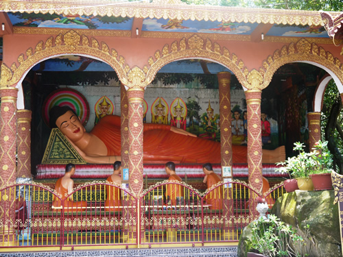 Cambodian Buddhist monks in red garb worshipping at a temple with in from a reclining red female statue.