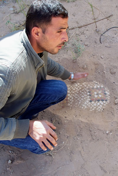 Man uneathing Mosaics at Madaba, Jordan with his hand.