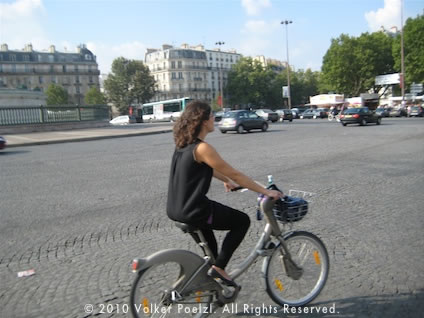 A man biking in Paris on the cobblestone square of Place de la Bastille.