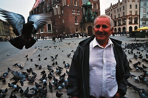 A smiling local man amid hundreds of pigeons in Krakow, Poland.