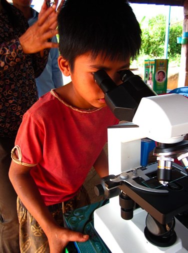 Child studying what he sees in a microscope in Cambodia.
