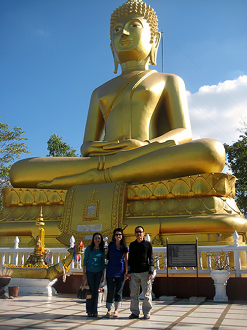 Author standing in front of a giant golden Buddha in Thailand with host parents.